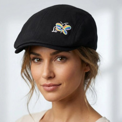 Modelo luciendo boina negra con diseño, donde destaca el logo de la libélula con los colores del arco iris