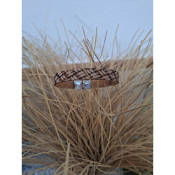 Pulsera de cuero grabado marrón colocada sobre un jarrón de esparto.