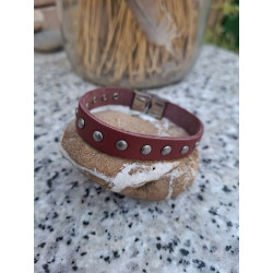 Pulsera de piel granate con tachuelas redondas sobre una piedra.