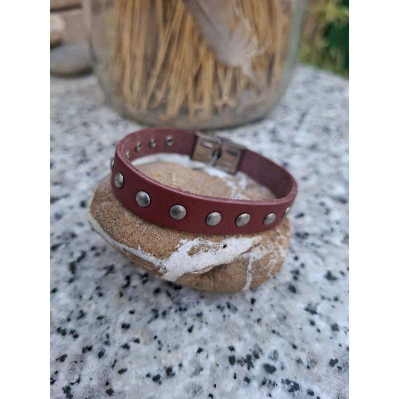 Pulsera de piel granate con tachuelas redondas sobre una piedra.