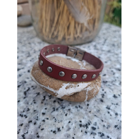 Pulsera de piel granate con tachuelas redondas sobre una piedra.