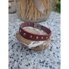 Pulsera de piel granate con tachuelas redondas sobre una piedra.