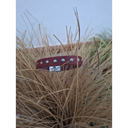 Primer plano de pulsera de piel granate con tachuelas redondas, en jarrón de esparto.