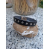 Pulsera de piel negra con tachuelas redondas sobre una piedra.