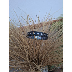 Primer plano de pulsera de piel negra con tachuelas redondas, sobre un jarrón de esparto.