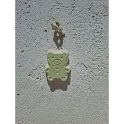 Adorno colgante de osito pequeño de cemento blanco de día fijado en una pared blanca exterior.