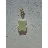 Adorno colgante de osito pequeño de cemento blanco de día fijado en una pared blanca exterior.