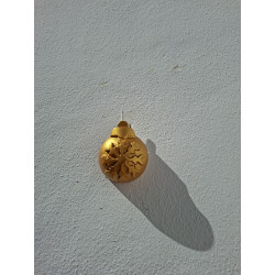 Esfera navideña de cemento pintada en oro con relieve de copo de nieve colgada en la pared de día.