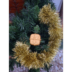 Adorno navideño con silueta de paquete de regalo en cemento color oro colgado en el árbol de Navidad.