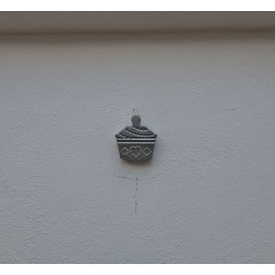 Adorno de cupcake de cemento pintado a mano con relieve estriado colgado en una pared texturizada blanca de día.