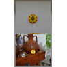 Adorno de girasol de cemento pintado a mano colgado en pared blanca y apoyado junto a una vasija rústica de barro.