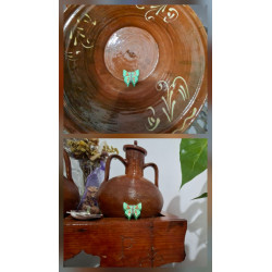 Adorno de mariposa de cemento pintado a mano color verde colocado en lebrillo tradicional y junto a vasija de barro rústica.