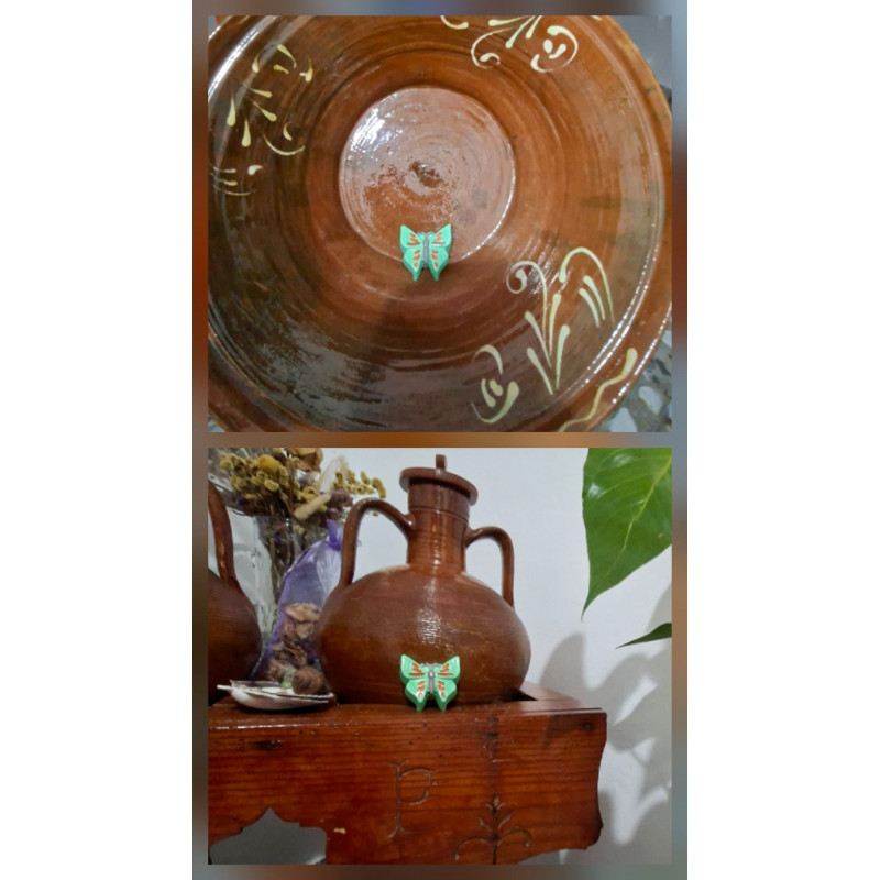 Adorno de mariposa de cemento pintado a mano color verde colocado en lebrillo tradicional y junto a vasija de barro rústica.