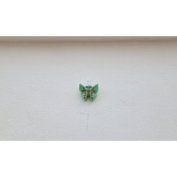 Adorno de mariposa de cemento verde pintado a mano colgado de forma individual en una pared blanca exterior.