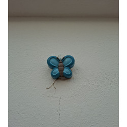 Adorno de mariposa de cemento azul intenso pintado a mano colgado verticalmente en una pared blanca exterior.