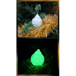 Adorno bola de Navidad de cemento fosforescente con relieve de copo de nieve de día en abeto y brillando color verde de noche.