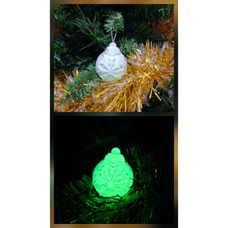 Adorno bola de Navidad de cemento fosforescente con relieve de copo de nieve de día en abeto y brillando color verde de noche.