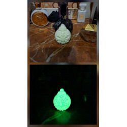 Adorno bola de Navidad de cemento fosforescente con copo de nieve mostrando su diseño de día y su brillo verde sobre mármol.