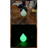 Adorno bola de Navidad de cemento fosforescente con copo de nieve mostrando su diseño de día y su brillo verde sobre mármol.