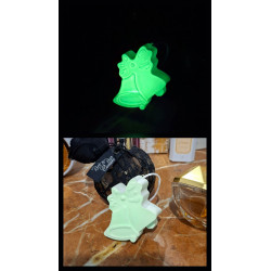Adorno de campanas de Navidad de cemento fosforescente con lazo mostrando su brillo verde y su diseño de día sobre mármol.