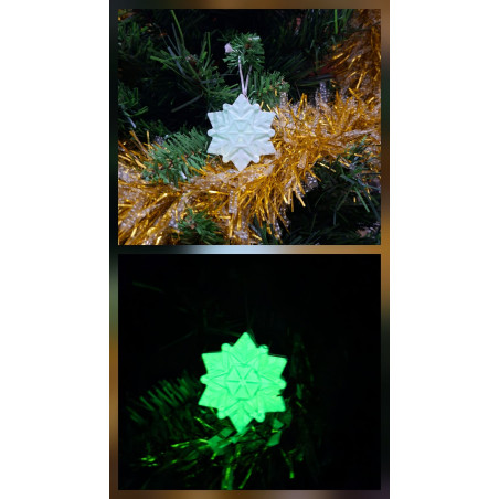 Adorno estrella copo de nieve de cemento fosforescente de día colgado en el abeto y mostrando su brillo verde en la oscuridad.