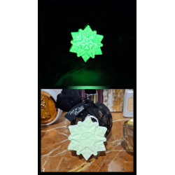 Adorno estrella copo de nieve de cemento fosforescente mostrando su brillo verde y su diseño de día sobre mármol.