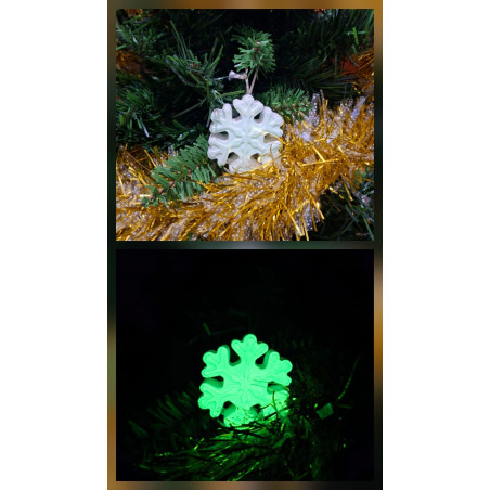 Adorno copo de nieve clásico de cemento fosforescente de día colgado en el abeto navideño y mostrando brillo verde en oscuridad.