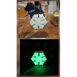 Adorno de copo de nieve clásico de cemento fosforescente mostrando su diseño de día y su brillo verde sobre mármol.