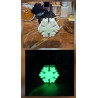 Adorno de copo de nieve clásico de cemento fosforescente mostrando su diseño de día y su brillo verde sobre mármol.