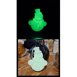 Adorno muñeco de nieve de cemento fosforescente mostrando su brillo verde y su diseño de día sobre mármol.