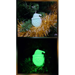 Adorno Papá Noel de cemento fosforescente de día colgado en el abeto navideño y mostrando su brillo verde en la oscuridad.