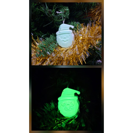 Adorno Papá Noel de cemento fosforescente de día colgado en el abeto navideño y mostrando su brillo verde en la oscuridad.