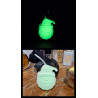 Adorno Papá Noel de cemento fosforescente mostrando su brillo verde y su diseño de día junto a frascos de perfume sobre mármol
