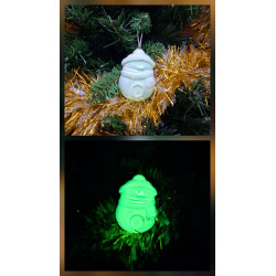 Adorno Papá Noel de cemento fosforescente modelo redondeado colgado en el abeto navideño y mostrando su brillo verde nocturno.
