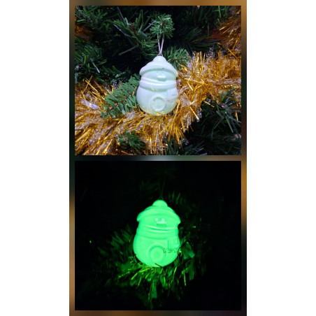 Adorno Papá Noel de cemento fosforescente modelo redondeado colgado en el abeto navideño y mostrando su brillo verde nocturno.