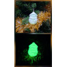 Adorno Papá Noel de cemento fosforescente modelo redondeado colgado en el abeto navideño y mostrando su brillo verde nocturno.