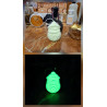 Adorno Papá Noel de cemento fosforescente modelo redondeado mostrando su brillo verde y su silueta de día sobre mármol.