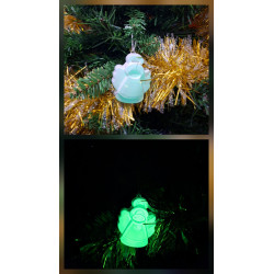 Adorno angelito Navidad de cemento fosforescente de día colgado en abeto junto a espumillón dorado y brillando verde de noche.