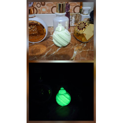 Adorno bola Navidad de cemento fosforescente con líneas diagonales mostrando su diseño de día y su brillo verde en la oscuridad.