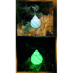 Adorno bola Navidad de cemento fosforescente con líneas diagonales de día en el abeto y brillando verde de noche.