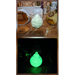 Adorno bola Navidad de cemento fosforescente con relieve de espirales mostrando su diseño de día y brillo verde en la oscuridad.