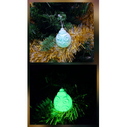 Adorno bola Navidad de cemento fosforescente con espirales de día en el abeto y brillando verde de noche.