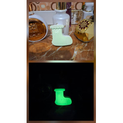 Adorno bota Navidad de cemento fosforescente mostrando su diseño de día junto a perfumes y su brillo verde en la oscuridad.