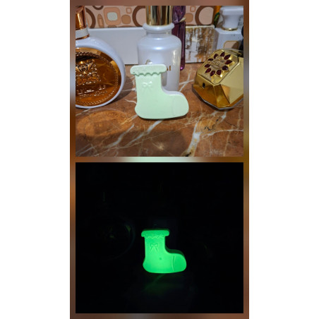 Adorno bota Navidad de cemento fosforescente mostrando su diseño de día junto a perfumes y su brillo verde en la oscuridad.