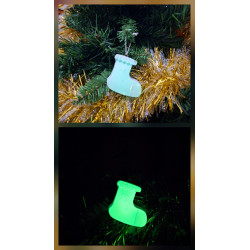 Adorno bota Navidad de cemento fosforescente con lazo de día en el abeto junto a espumillón dorado y brillando verde de noche.