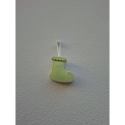 Adorno bota Navidad de cemento fosforescente con relieve de lazo colgado de forma vertical en una pared blanca exterior.
