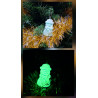 Adorno muñeco nieve de cemento fosforescente modelo bombín de día en el abeto y brillando verde de noche.