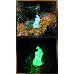 Adorno Papá Noel de cemento fosforescente con gorro inclinado de día en el abeto y brillando verde de noche.
