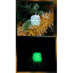 Adorno regalo de Navidad de cemento fosforescente con lazo de día en el abeto y brillando verde de noche.