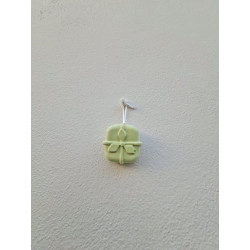 Adorno regalo de Navidad de cemento fosforescente con relieve de lazo colgado de forma vertical en una pared blanca exterior.